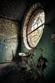 an old bathroom with a round window in the wall and peeling paint on the walls