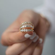 a woman's hand holding two gold rings with white diamonds on top and one in the middle