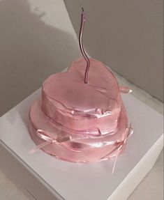 a pink frosted cake sitting on top of a white box with ribbon around it