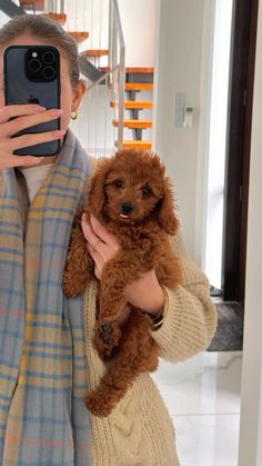 a woman taking a selfie while holding a brown poodle in her arms and looking at the camera