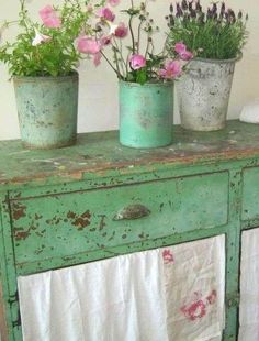 three potted plants sit on top of an old green cabinet with white drapes