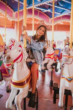 a woman sitting on top of a merry go round at an amusement park with horses