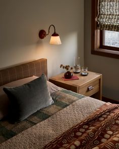 a bed sitting under a window next to a night stand with two lamps on it