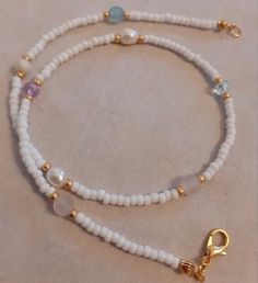 a white beaded bracelet with gold clasps and charms on it's side