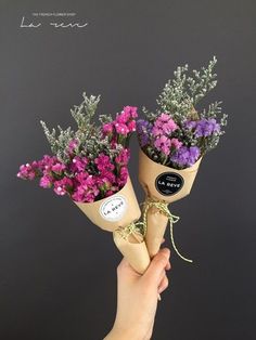 two hands holding flowers in paper cones with the words love written on them and tied to each other