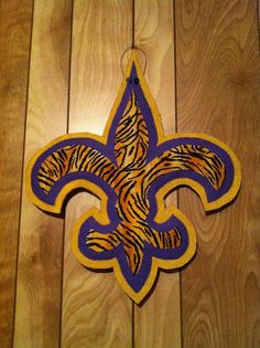 a purple and yellow fleur de lis hanging on a wooden wall