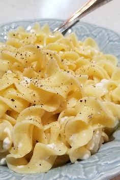 a blue plate topped with macaroni and cheese covered in seasoning next to a fork