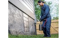 a man in blue coveralls holding a bucket and spraying water on the side of a house