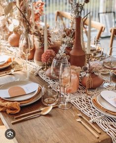 a dining table set with place settings, plates and vases on top of it