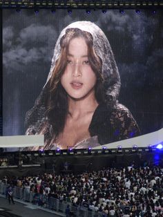 a large screen with a woman's face on it in front of an audience