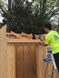 a man standing on a ladder next to a wooden shed with the door open and tools in it