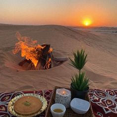 a desert setting with food and drinks on the table in front of an open fire pit