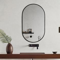 an oval mirror hangs on the wall next to a vase with a plant in it