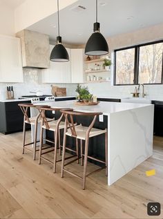 a kitchen with black and white cabinets, an island table and three stools in it