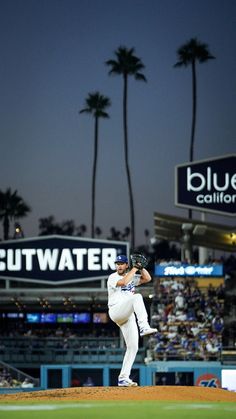 a baseball player pitching a ball on top of a field in front of palm trees