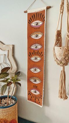 an orange wall hanging with all seeing eyes on it next to a potted plant