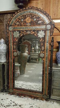 an ornate wooden mirror sitting on top of a table next to vases and other decorative items