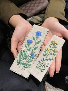 two embroidered bookmarks in the shape of flowers are being held by someone's hands