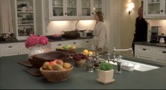 two people standing in a kitchen next to a counter with fruit and vegetables on it