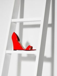 red high heeled shoes sitting on top of a white shelf next to a ladder