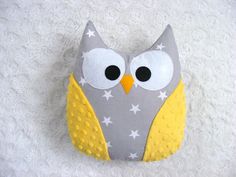 an owl pillow with yellow and gray stars on it's face, sitting on a white blanket