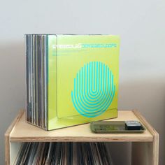 a stack of vinyl records sitting on top of a wooden shelf next to a cell phone