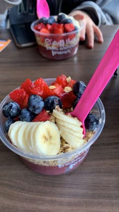 a bowl of fruit and yogurt with a pink plastic spoon in it on a table