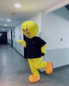 a person in a yellow bird costume standing next to a white wall and gray floor