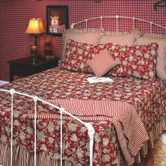 a bed with red and white bedspread sitting next to a lamp on a table