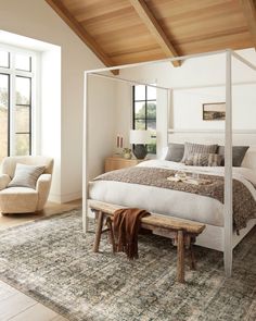 a bedroom with a canopy bed, chair and rug on the floor in front of large windows