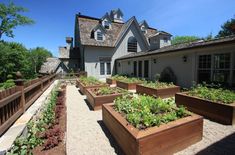 an outdoor garden area with raised beds and wooden planters in front of a house