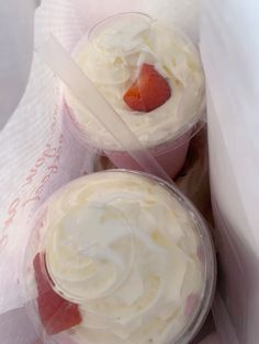 two desserts in plastic cups with strawberries on top and white frosting around them