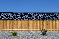 a wooden fence with metal panels on top and plants growing in the gravel behind it