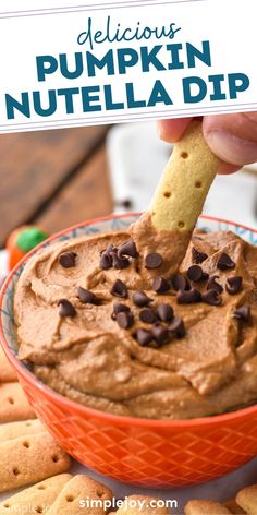 a hand dipping a cracker into a bowl of pumpkin nutella dip with chocolate chips