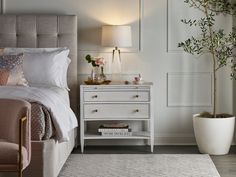 a bedroom with a bed, nightstand and potted plant on the side table next to it