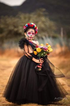 a woman in a black dress with flowers on her head and makeup painted to look like a skeleton