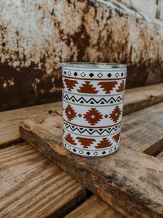 a white and brown cup sitting on top of a wooden table next to a rusted wall