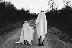 two people dressed as ghost walking down a dirt road