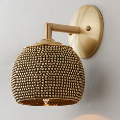 a wall light that is on the side of a white wall and has gold dots covering it