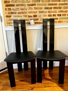 two black chairs sitting on top of a hard wood floor next to a brick wall