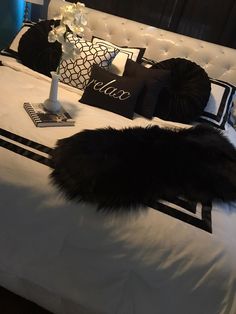 a white bed with black and white pillows on it's headboard, next to a vase filled with flowers