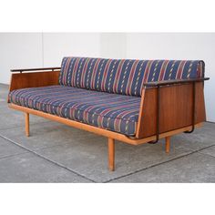 a blue and red striped couch sitting on top of a cement floor next to a white wall