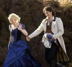 a man and woman dressed in period clothing walking down a hill together, one holding the other's hand