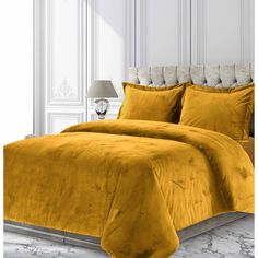 a bed with yellow comforter and pillows in a white room next to a lamp