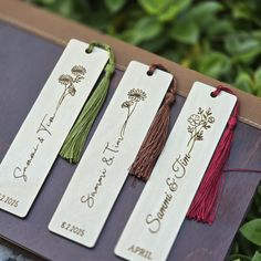 three bookmarks with names and tassels on them sitting on top of a table