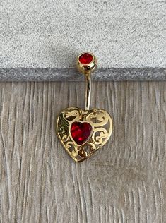 a gold heart shaped belly ring with two red stones on the top and bottom part