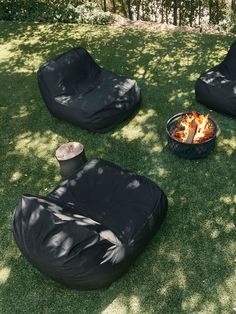 black bean bag chairs sitting in the grass near a fire pit and trashcans