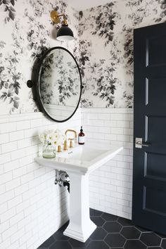 a bathroom with black and white wallpaper has a sink, mirror, and door