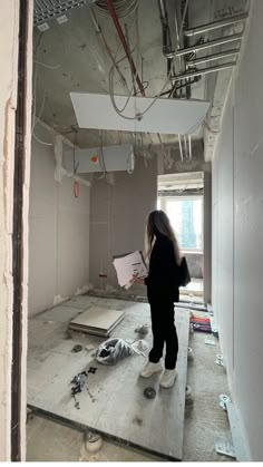 a woman standing in an unfinished room looking at something on the floor