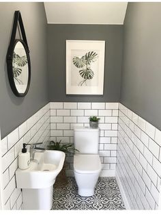 a white toilet sitting next to a sink in a bathroom under a framed plant on the wall